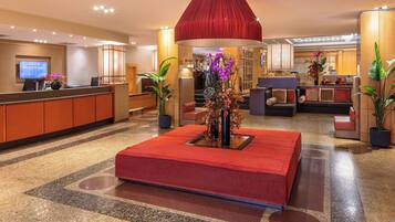 Un hall de hotel con mostrador de recepción, zona de estar y una gran pieza decorativa roja.
