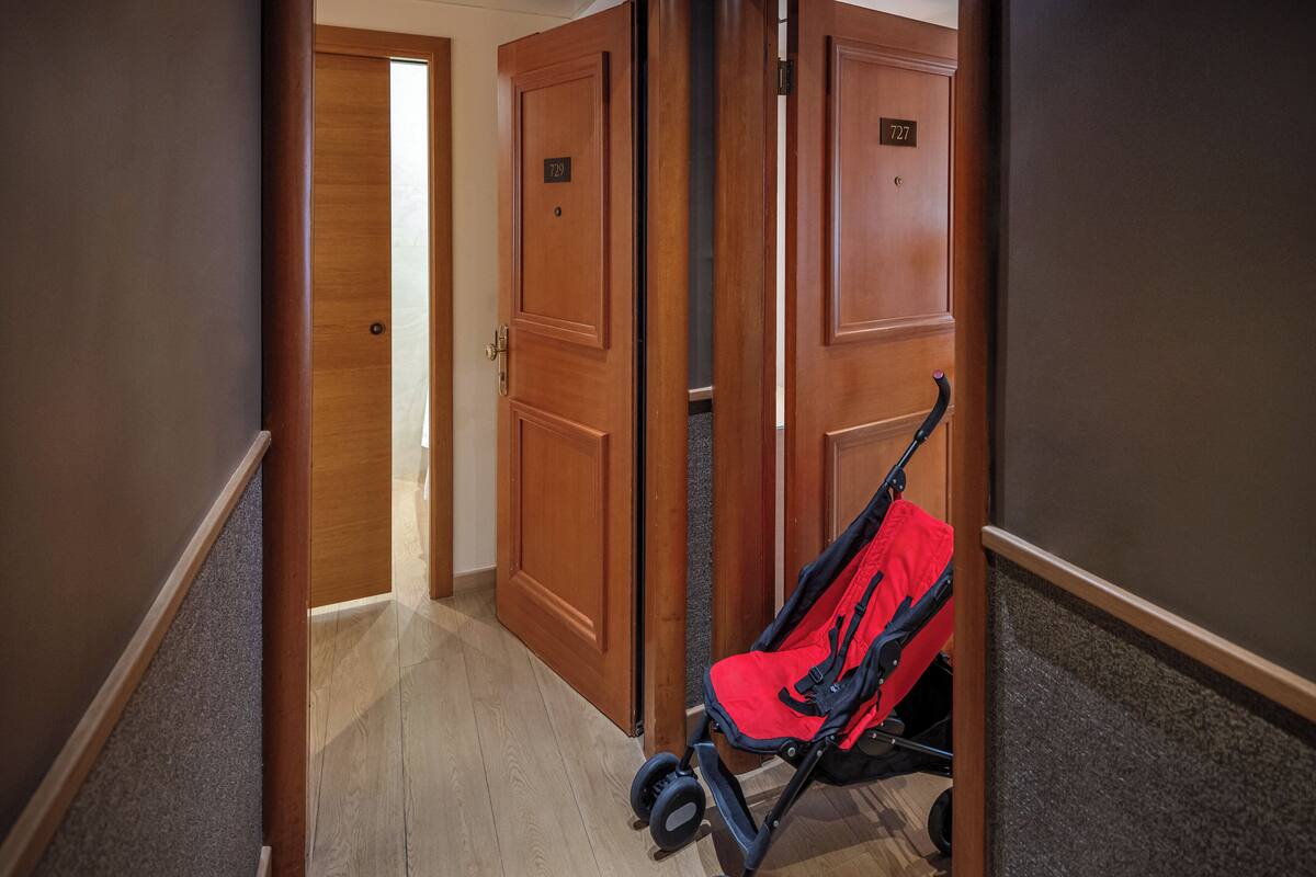 A hallway with wooden doors, one labeled 727, and a red stroller in the foreground.