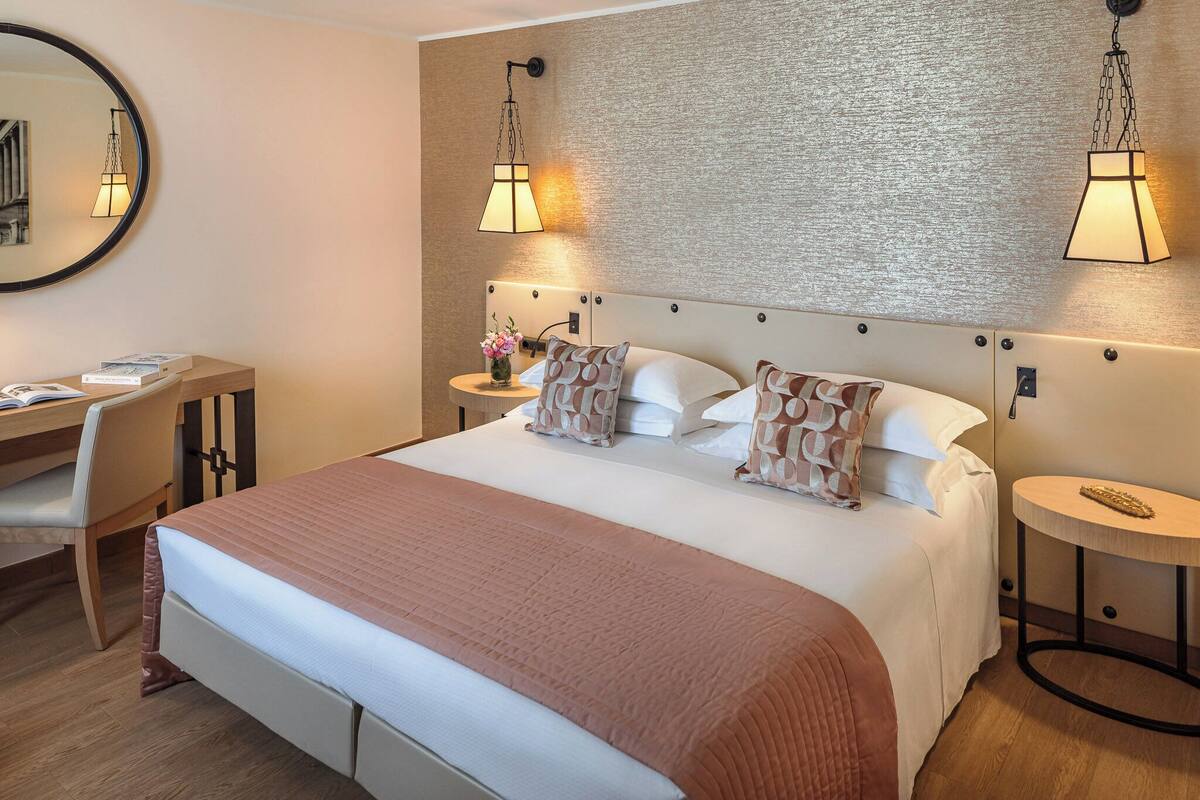 A neatly arranged hotel room with a large bed, a desk, and two bedside tables.