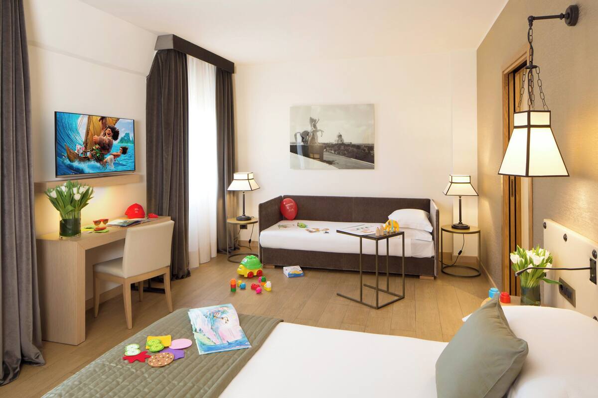 A hotel room with a bed, desk, chair, and artwork on the walls.