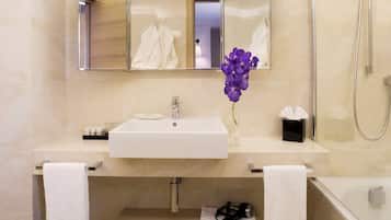 Un baño moderno con un lavamanos, espejo y ducha blancos. Hay toallas y artículos de aseo en la encimera.