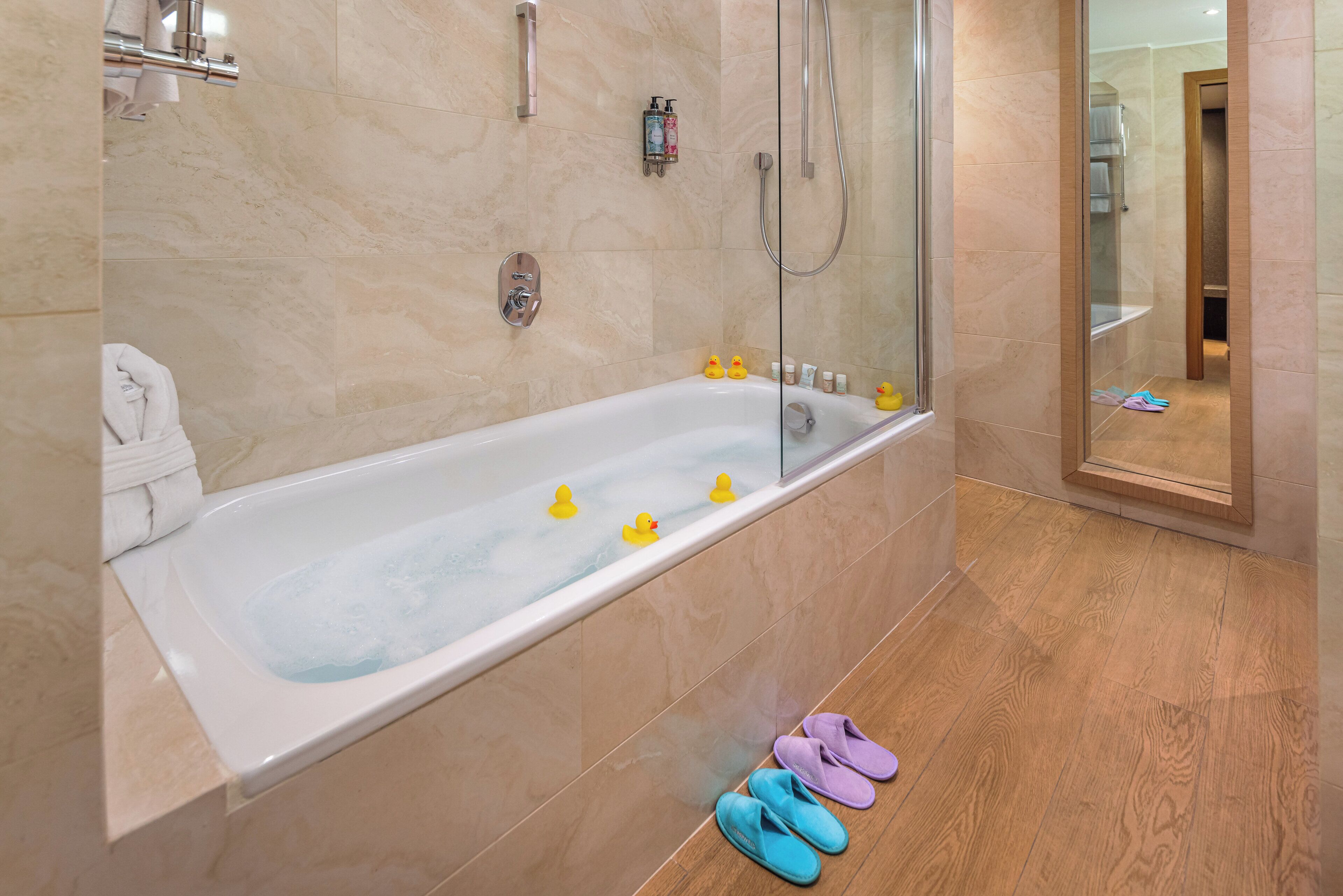 Un bagno moderno con una vasca da bagno ampia, cabina doccia in vetro e pavimento in legno.