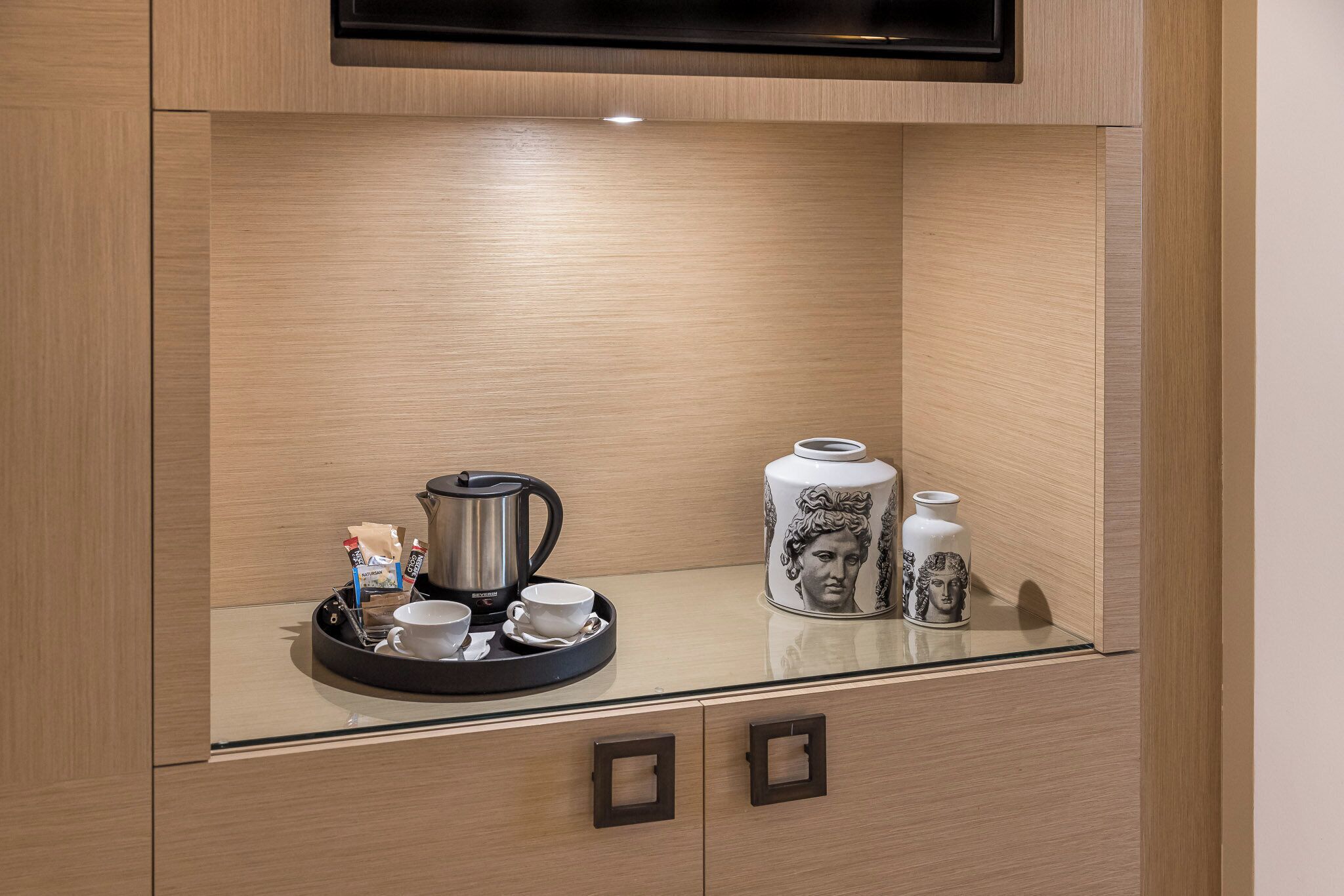 A modern kitchenette with a coffee maker, cups, and a tray.