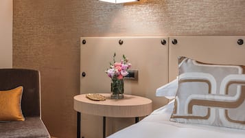A hotel room with a bed, a bedside table with a vase of flowers, a lamp, and a chair.