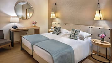 A hotel room with two beds, a desk, a chair, a round mirror, and two wall-mounted lamps.