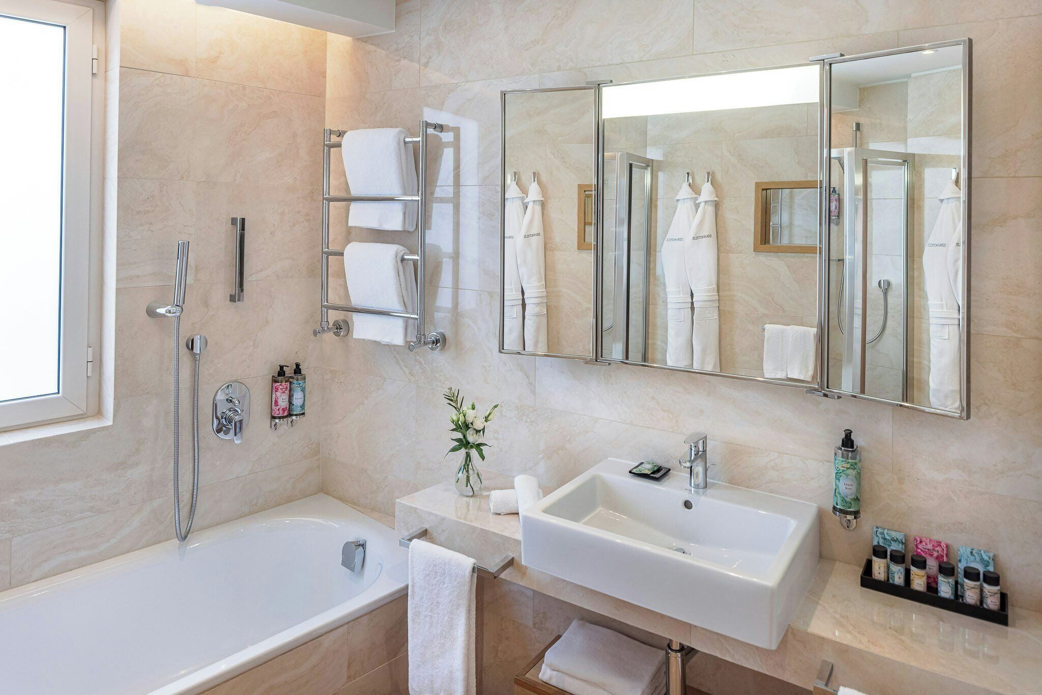 A modern bathroom with a bathtub, two sinks, a glass shower enclosure, and a large mirror.