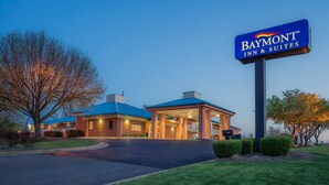 Un Baymont Inn & Suites con techo azul, entrada bien iluminada y entrada de acceso ajardinada.