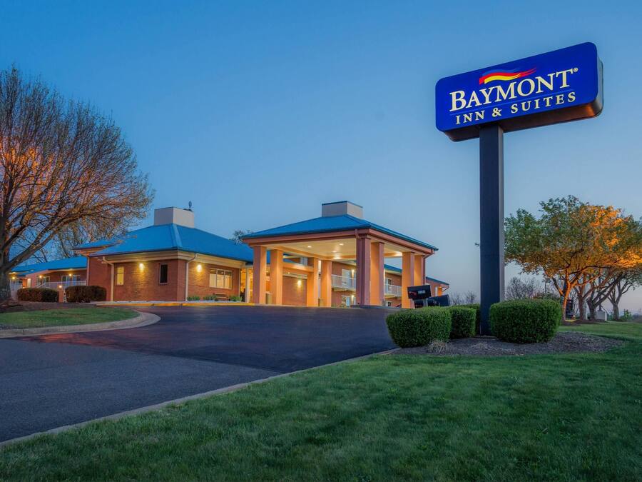 Un Baymont Inn & Suites con techo azul, entrada bien iluminada y entrada de acceso ajardinada.