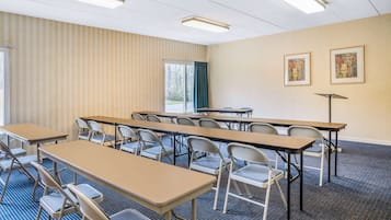 Una sala de conferències amb diverses taules i cadires, un finestral gran amb cortines, i dos quadres penjats a la paret.
