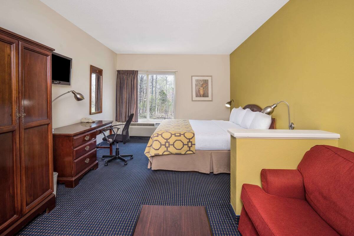 Una habitación de hotel con cama, escritorio, silla, armario y un sofá rojo.