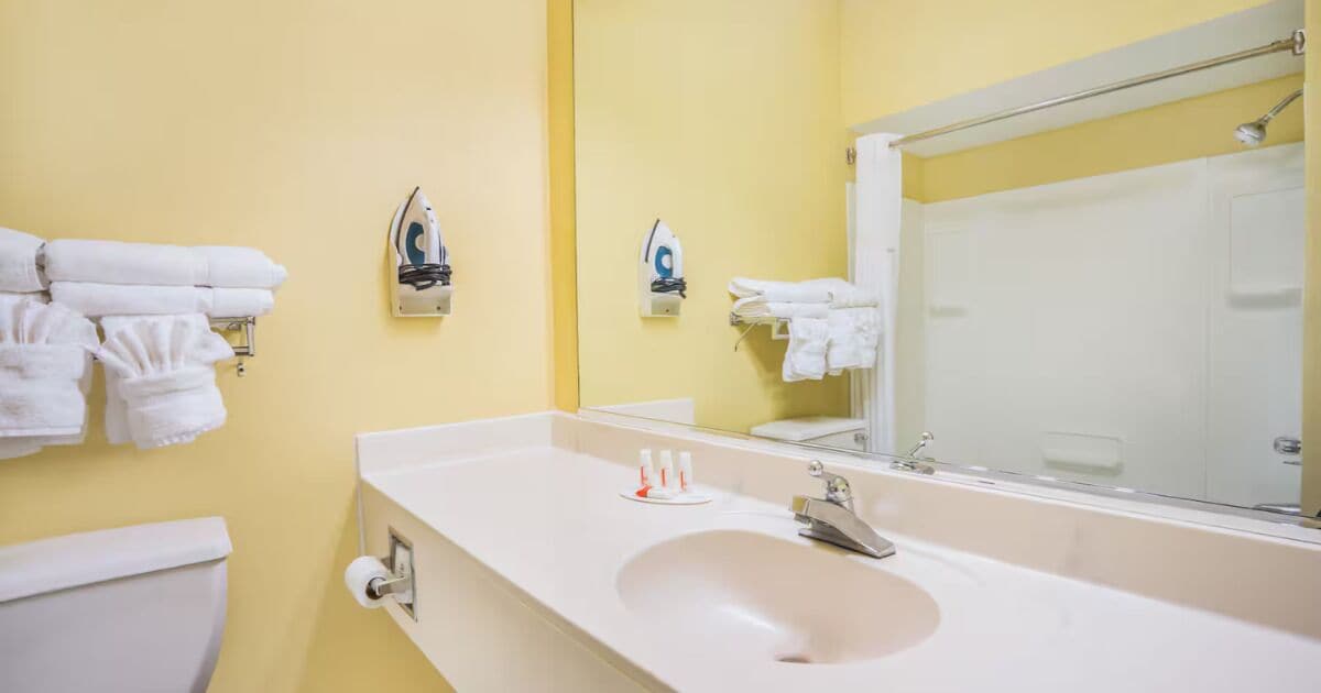 Un baño con pared amarilla, lavamanos blanco y dos planchas fijadas a la pared.