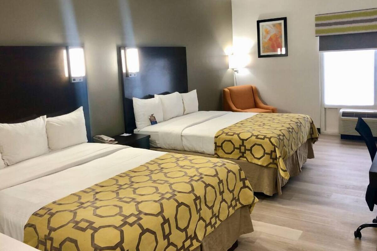 Habitación de hotel con dos camas, una silla, un escritorio y un ventanal.