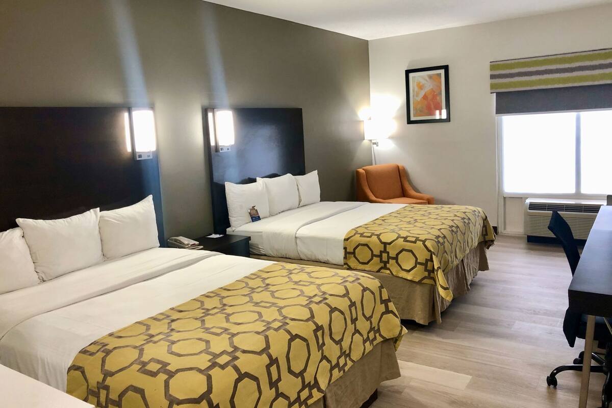 Una habitación de hotel con dos camas, un escritorio, una silla y una ventana.