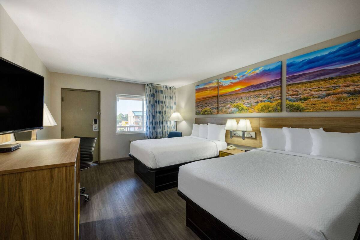 A hotel room with two beds, a desk, a TV, and a large painting on the wall.