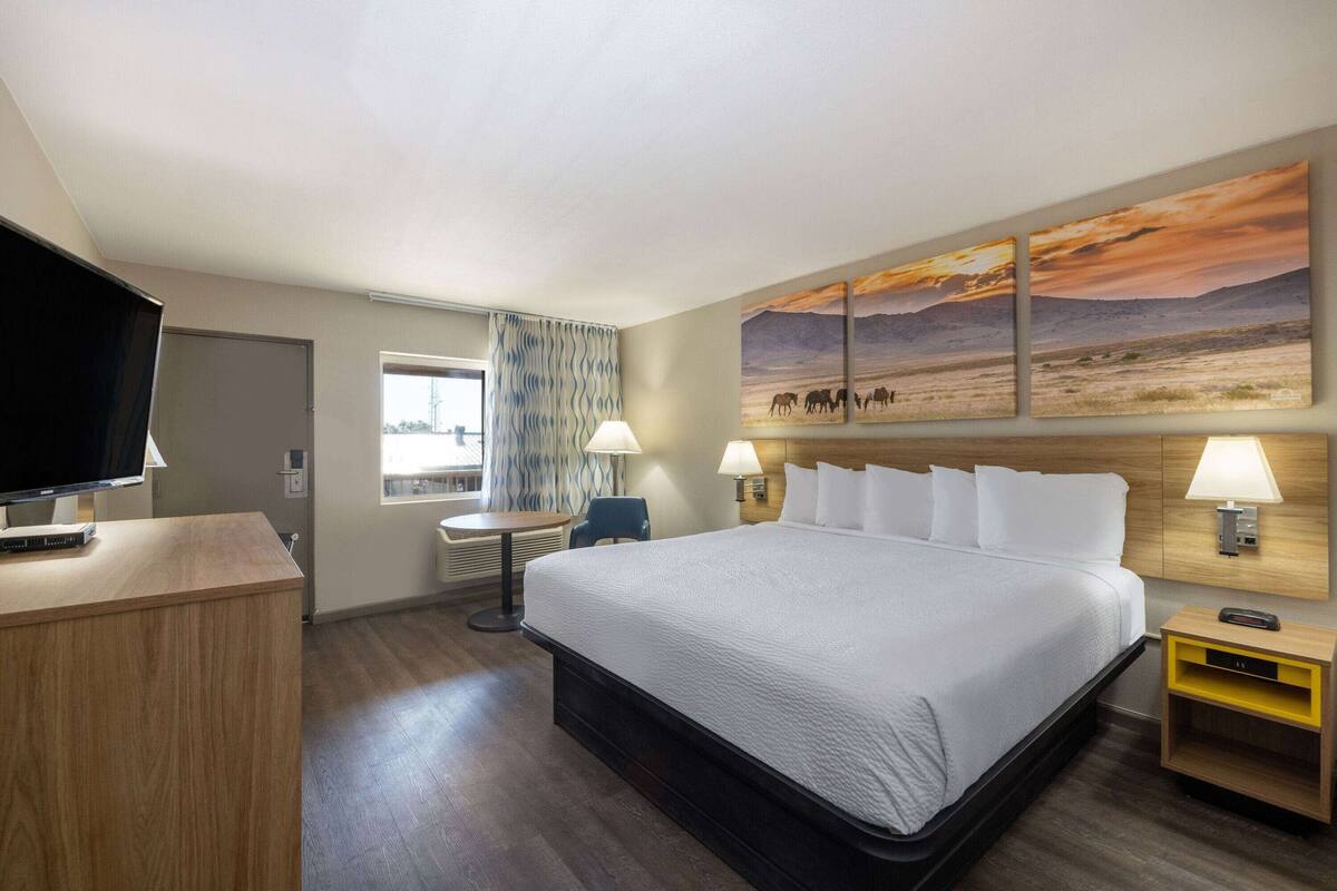A hotel room with a bed, a desk, a TV, and a painting on the wall.