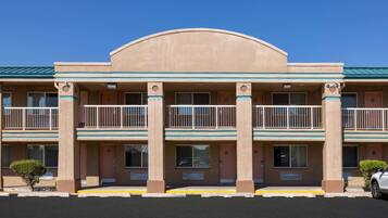 A multi-story hotel with a flat roof, balconies on each floor, and a parking lot in front.