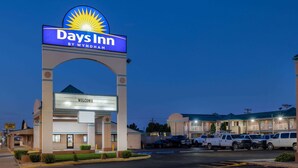 A Days Inn by Wyndham with a large arch entrance, parking area, and a row of motel buildings in the background. - Days Inn by Wyndham Roswell (Roswell)