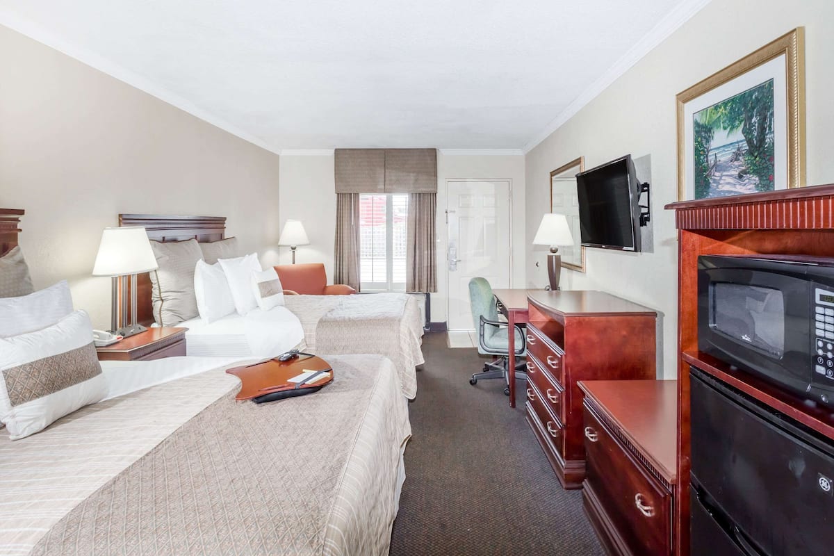 A hotel room with two beds, a desk, a television, and a fireplace.
