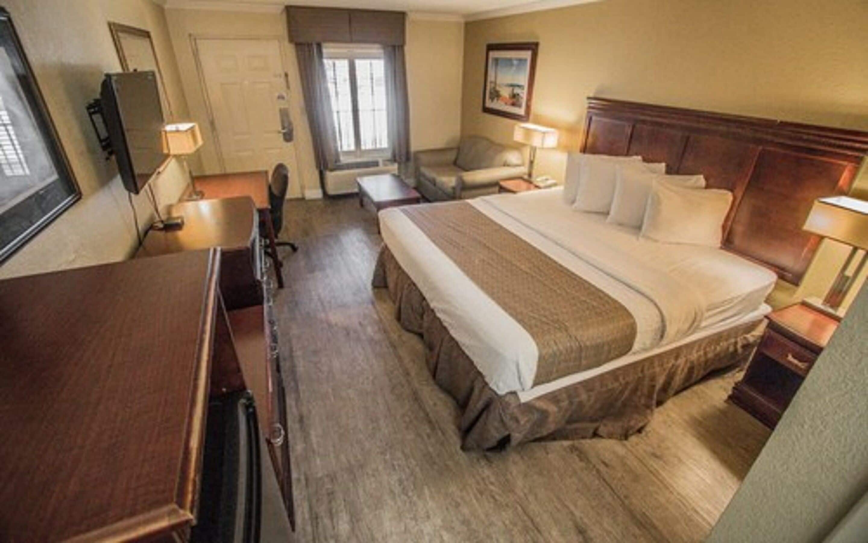 A hotel room with a large bed, a desk, a chair, a television, and a door.