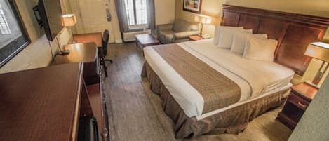 Una habitación de hotel con una cama grande, un escritorio, una silla, un televisor y una puerta.