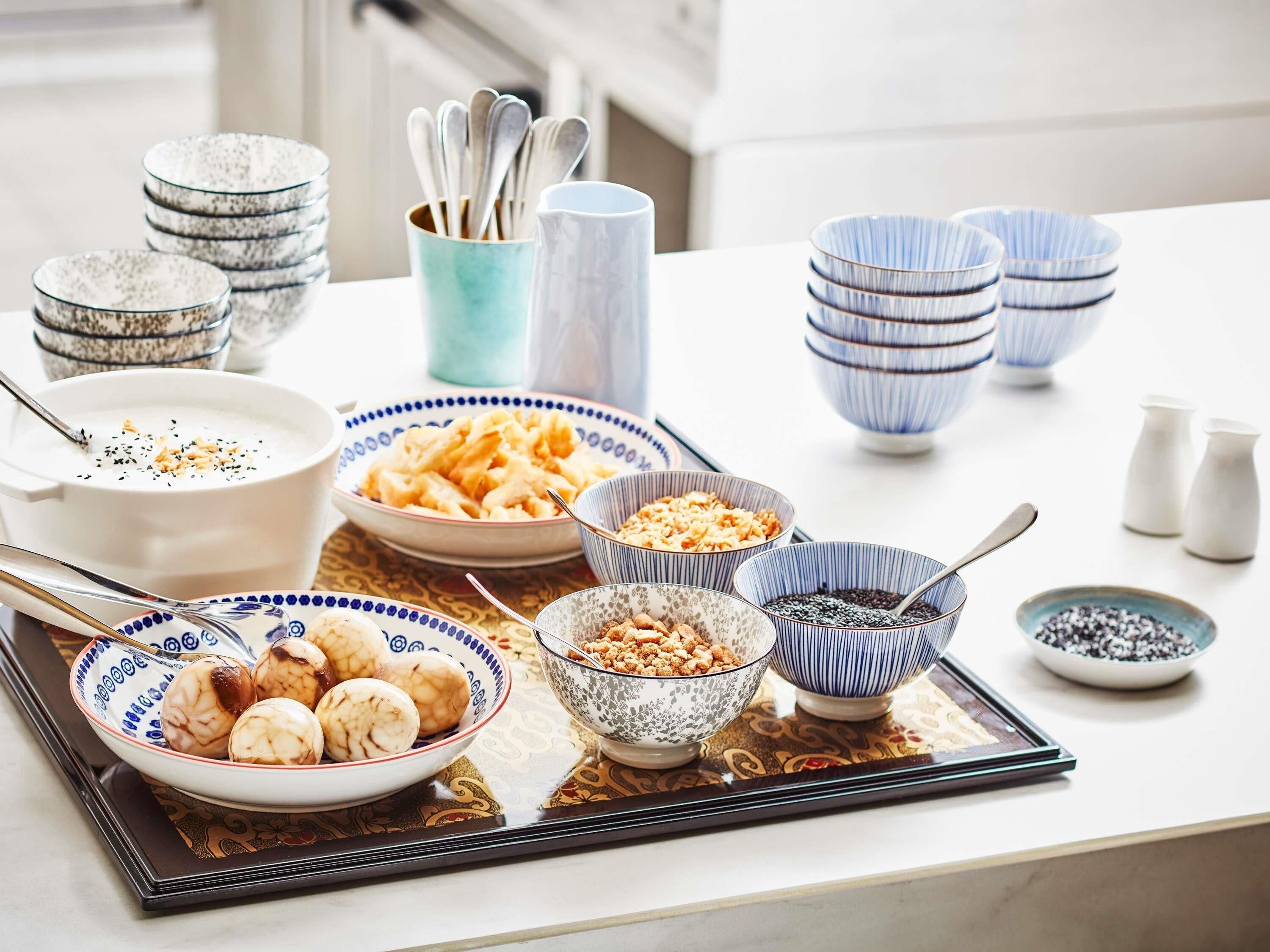 Una mesa de comedor con varios cuencos y platos de comida, incluyendo un tazón de sopa, un plato de dumplings y un cuenco de nueces.