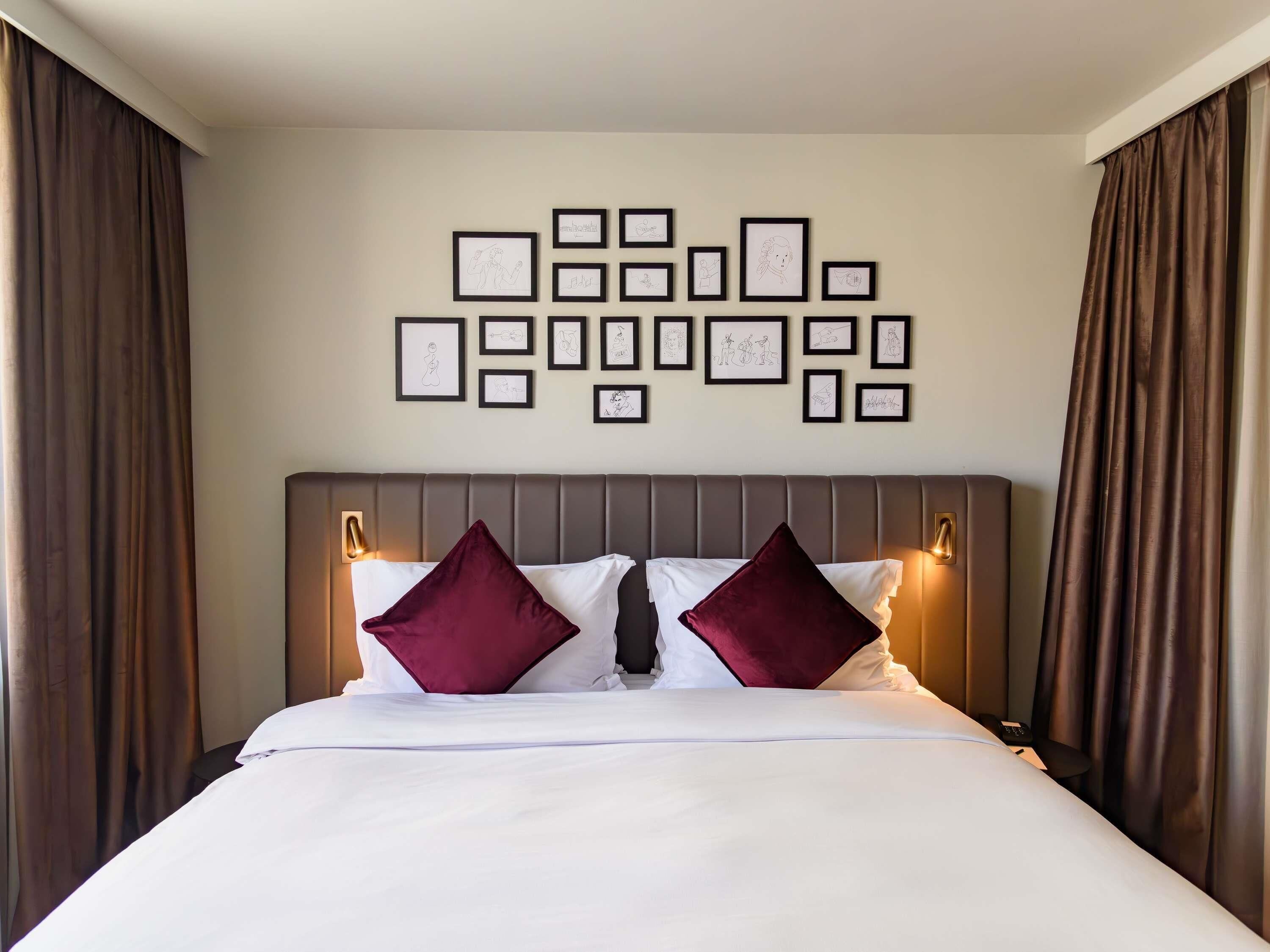 Een hotelkamer met een bed, twee kussens, een hoofdbord en een muur met ingelijste foto's.