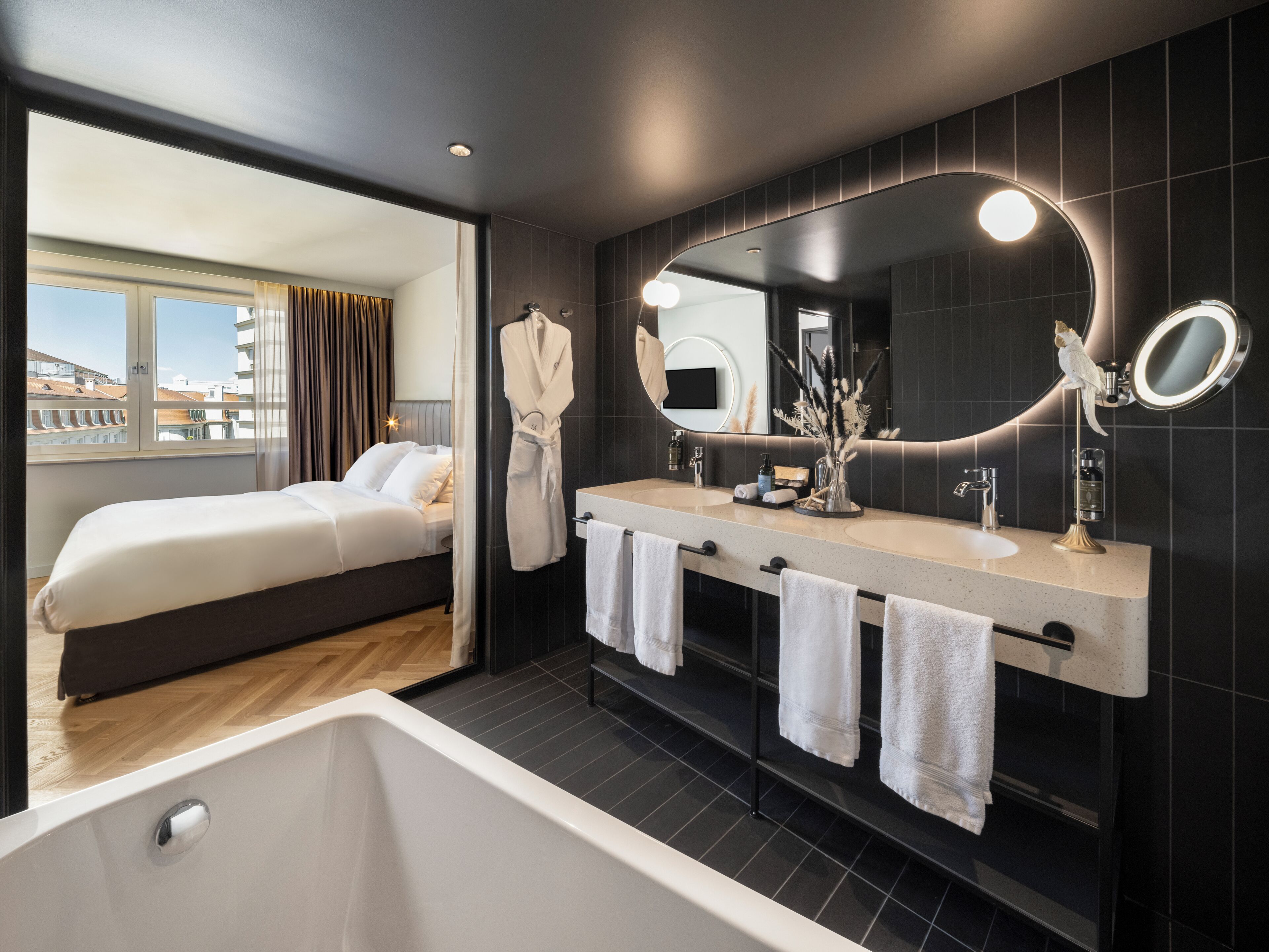 Ein modernes Hotelzimmer mit einem großen Bett, einem Badezimmer mit einer Badewanne und Blick auf die Stadt durch das Fenster.