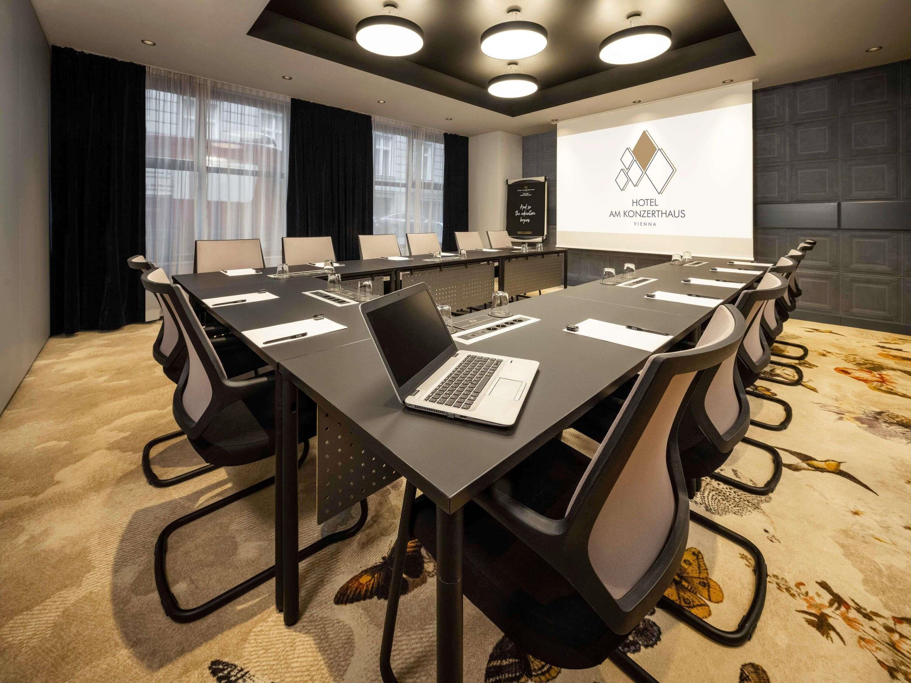 A conference room with a long table, chairs, a laptop, and a presentation screen.