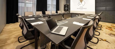 A conference room with a long table, chairs, a laptop, and a presentation screen.