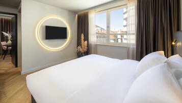 Et moderne hotelværelse med en stor seng, et rundt, vægmonteret TV, udsigt til bygninger gennem vinduet og trægulv.