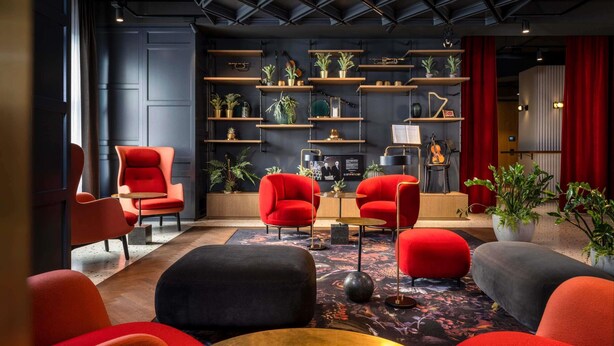 A modern lounge area with red and black chairs, a central table, and shelves with plants and decorative items. - Hotel Am Konzerthaus - MGallery Collection (Vienna)