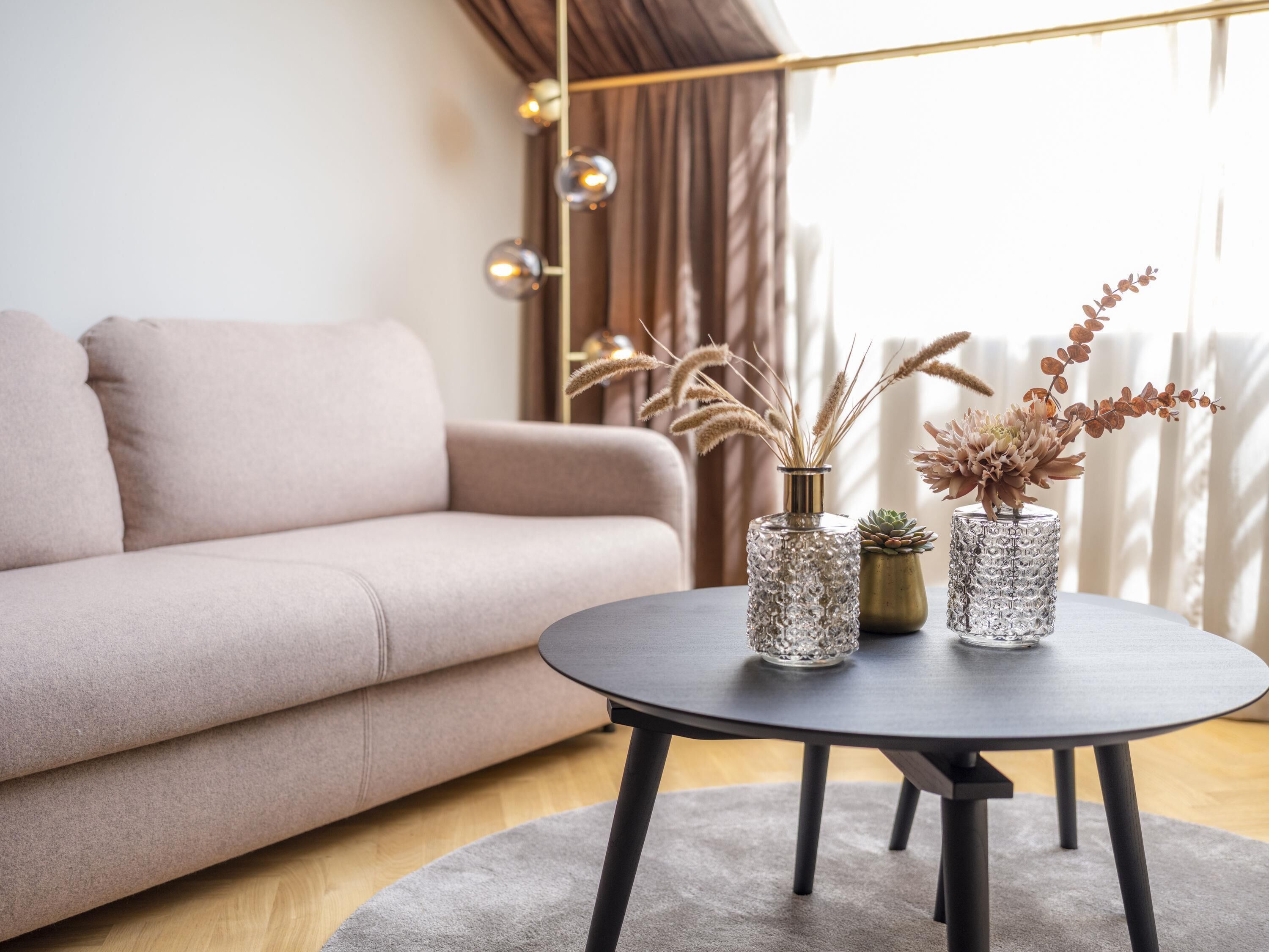 Een moderne woonkamer met een bank, een ronde tafel met vazen en een raam met gordijnen.