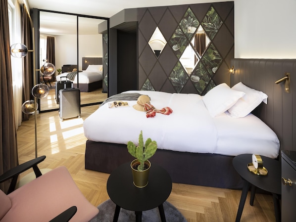 A hotel room with a bed, a small round table, a chair, a suitcase, and a potted plant. - Hotel Am Konzerthaus - MGallery Collection (Vienna)