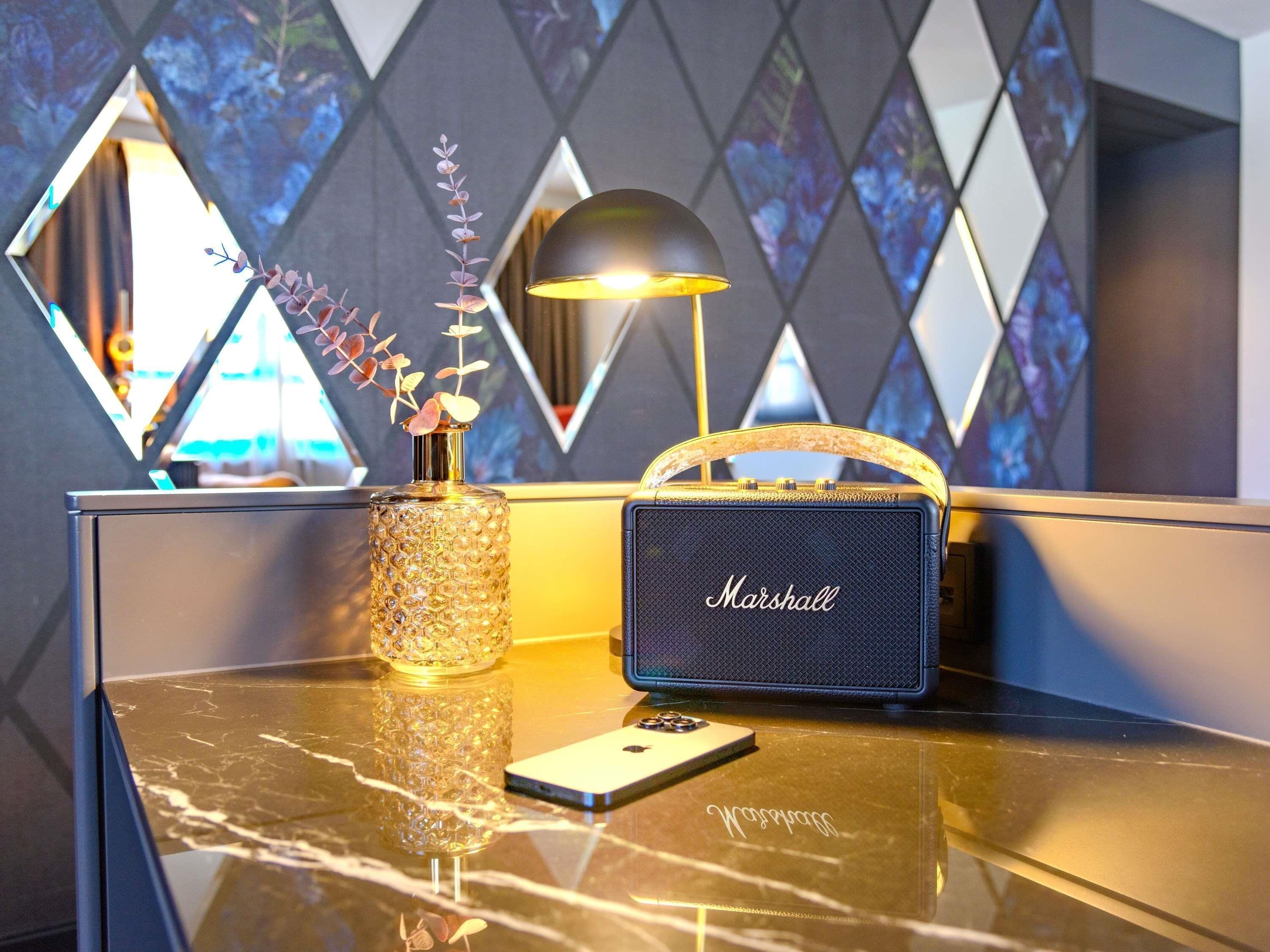 A marble table with a decorative vase, a Marshall speaker, and a smartphone.