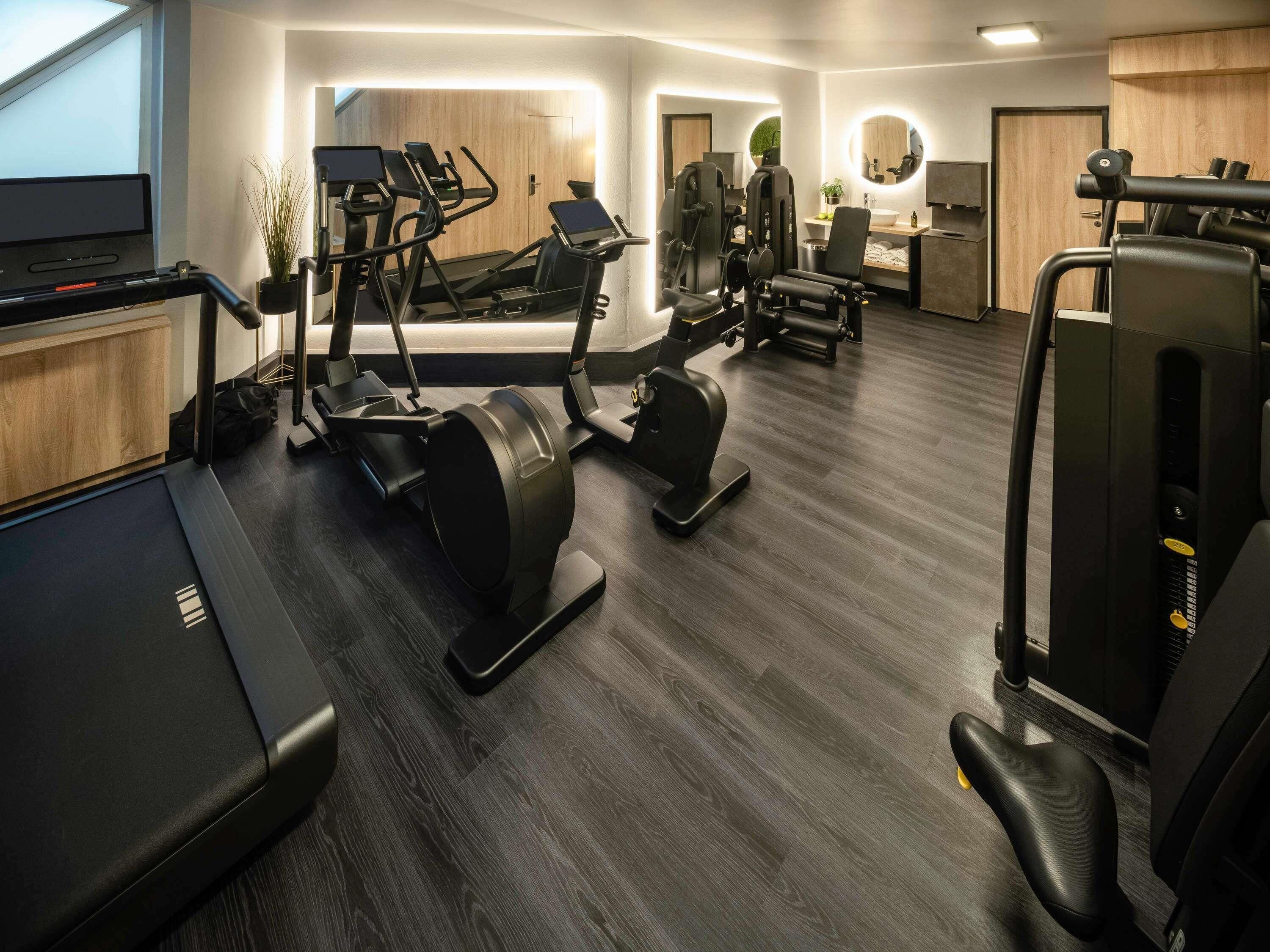 A modern gym with various cardio machines, a small desk area, and a mirror.