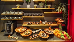 A variety of food and drink items displayed on wooden shelves and tables, with potted plants and a coffee machine. - Hotel Am Konzerthaus - MGallery Collection (Vienna)