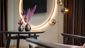 A modern interior with a round table, two vases with decorative items, a sofa, and a floor lamp with a circular light fixture. - Hotel Am Konzerthaus - MGallery Collection (Vienna)