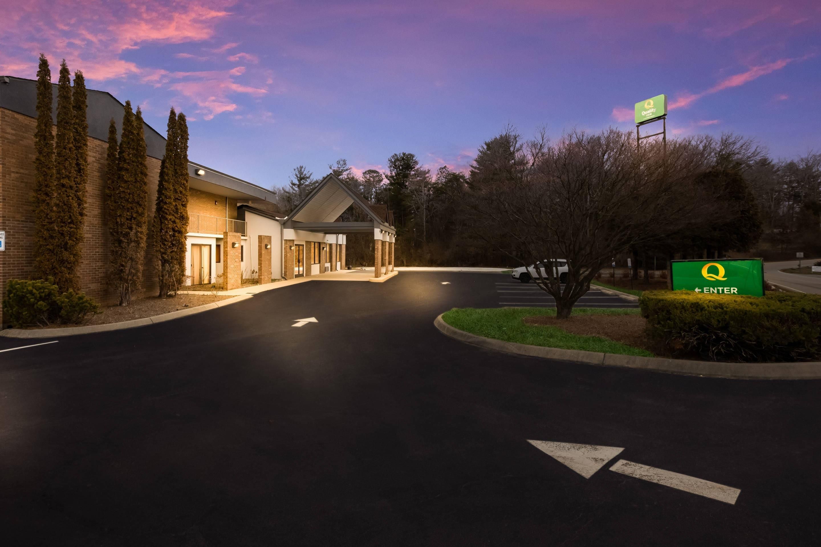 A hotel entrance with a parking lot, directional arrows, and a green sign with a yellow logo.