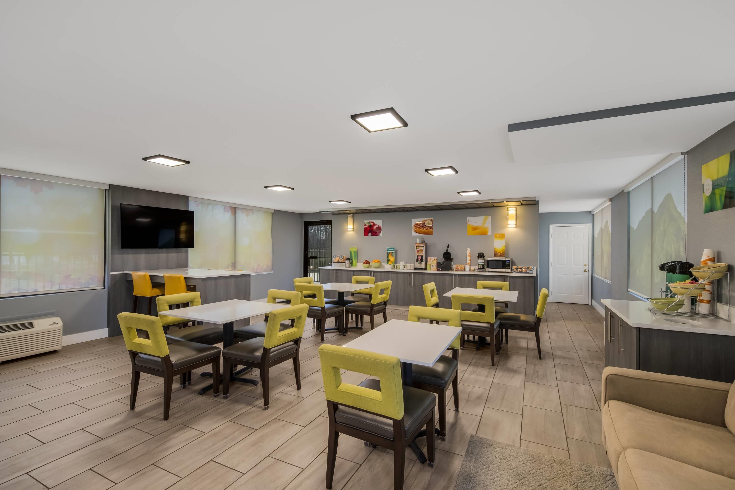 A modern dining area with multiple tables and chairs, a kitchen counter with various items, and a television mounted on the wall.