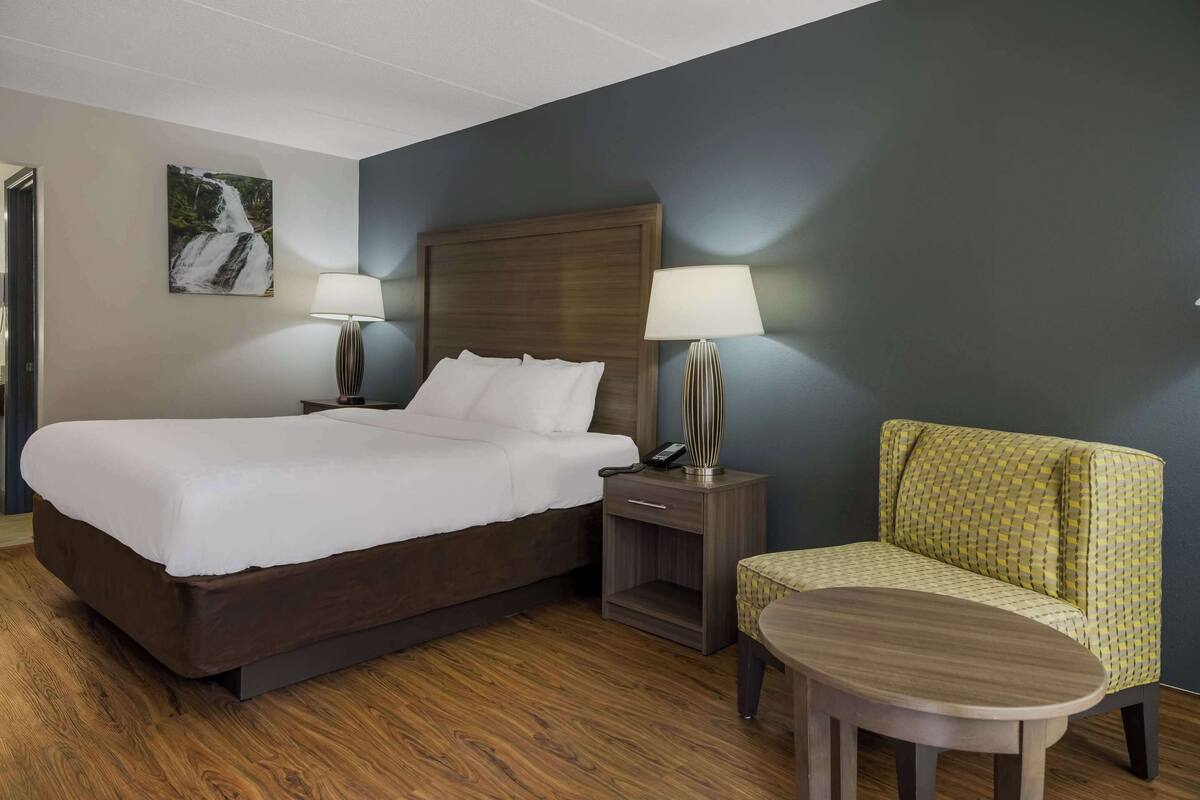 A hotel room with a large bed, two bedside tables with lamps, a small round table, and a green patterned armchair.