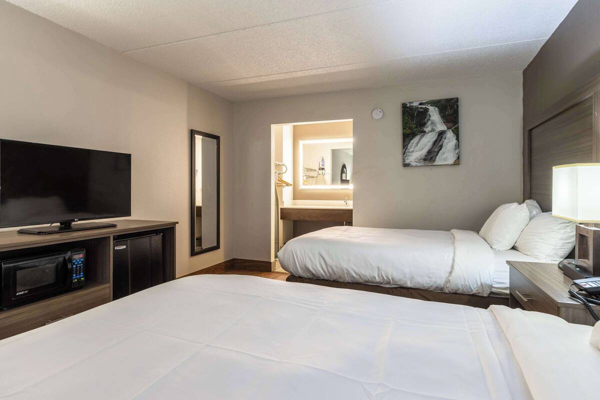 A hotel room with two beds, a TV, a microwave, and a bathroom visible through an open door.