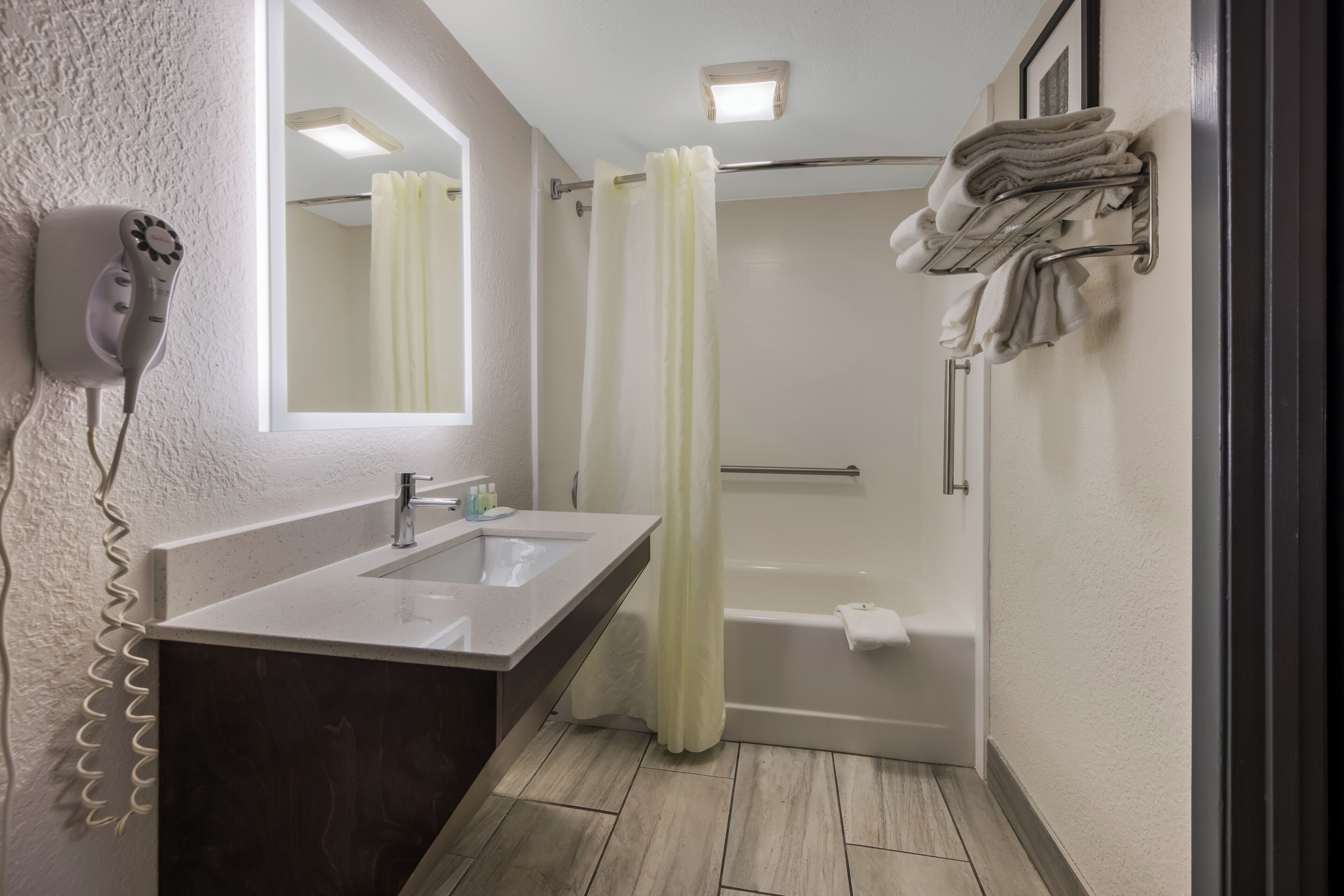 Baño con lavamanos, espejo, secador de pelo, cortina de ducha y toallas.