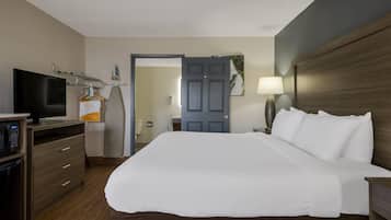 A hotel room with a bed, a TV, a desk with a computer, a lamp, and a door leading to a bathroom.