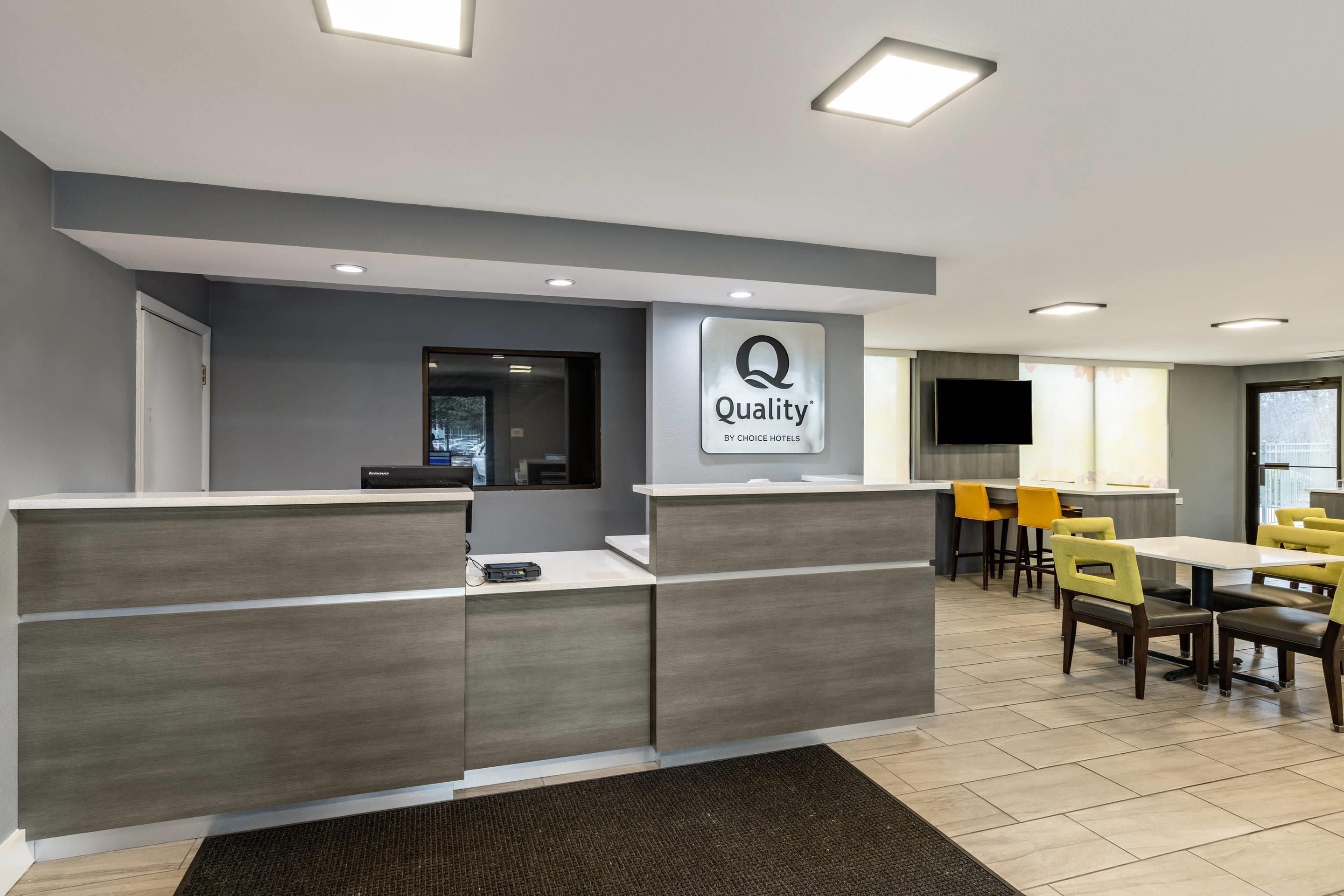 A hotel reception area with a modern design, featuring a reception desk, a television, and a seating area with yellow chairs.