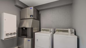 Un área de lavandería con calentador de agua, dispensador de agua en la pared y dos lavadoras de carga frontal.