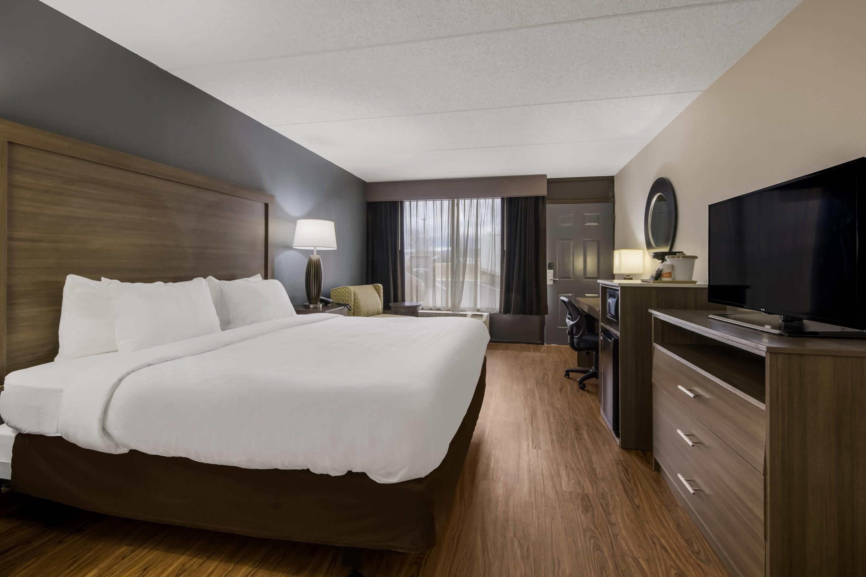 A hotel room with a large bed, a desk with a chair, a television, and a wardrobe.