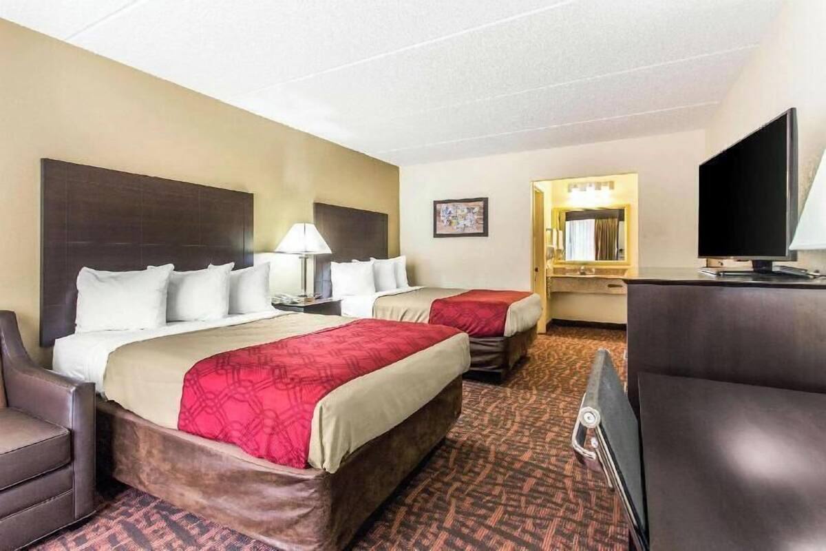 A hotel room with two beds, a desk, a chair, a television, and a mirror.