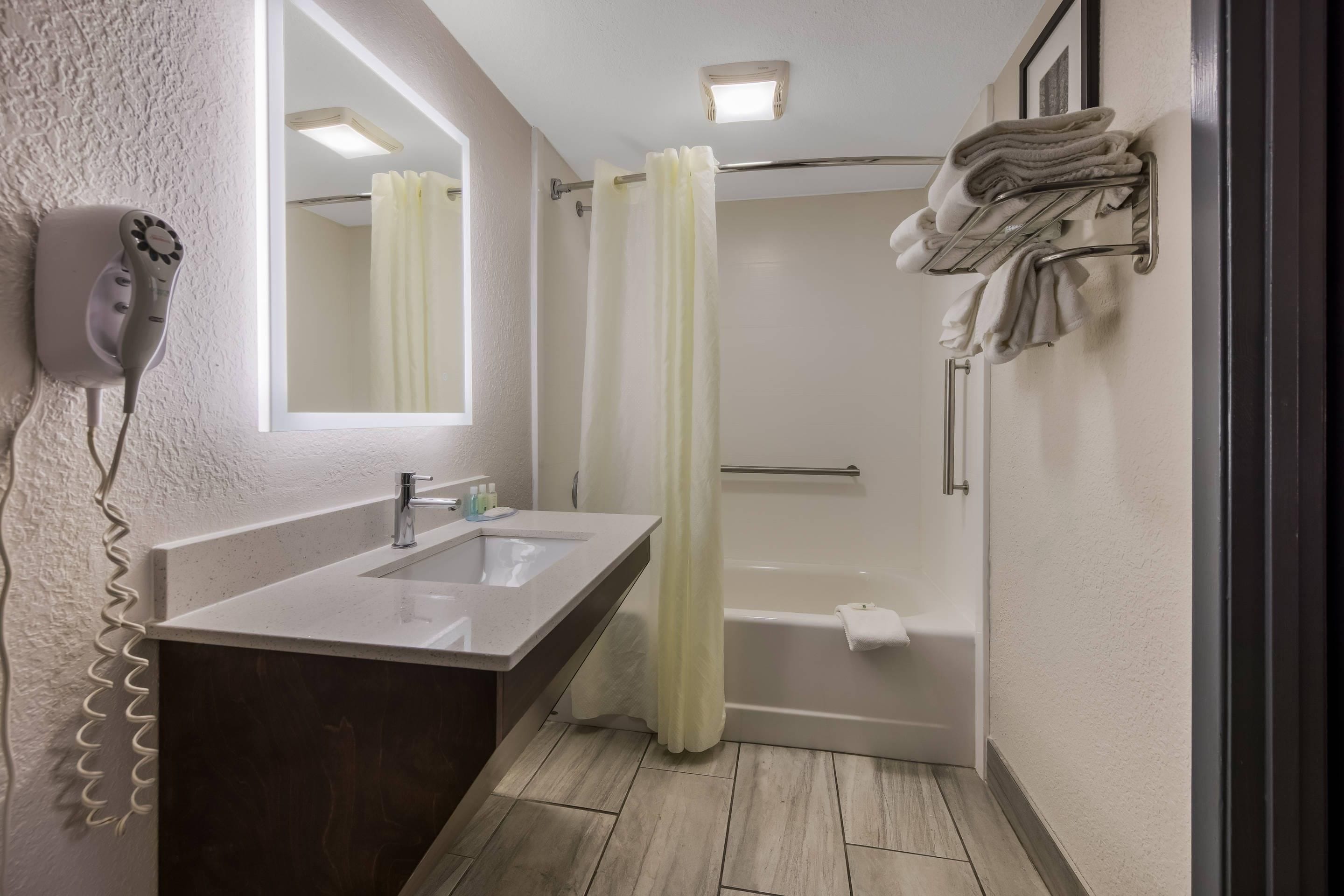 Ein Badezimmer mit Waschbecken, Spiegel, Dusche und Handtuchhalter.