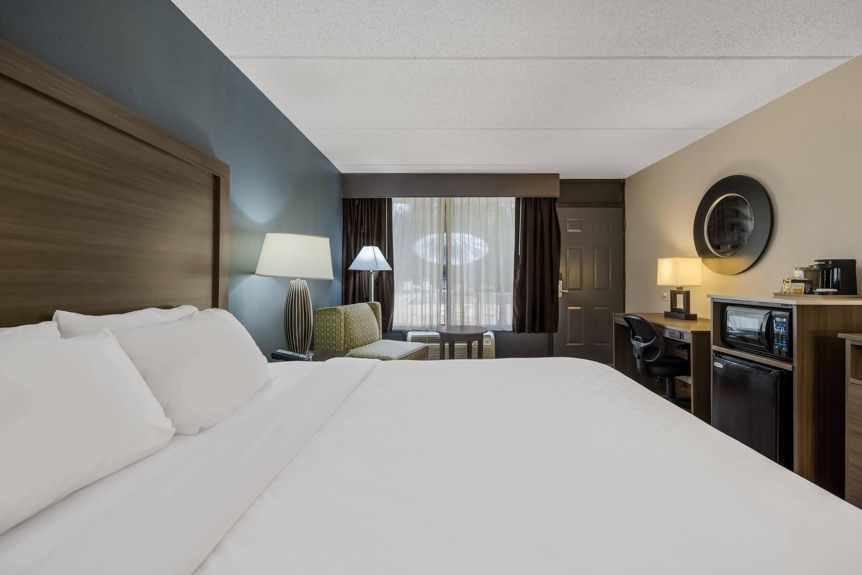 Quarto de hotel com uma cama grande, escrivaninha com computador, cafeteira e vista para o exterior.
