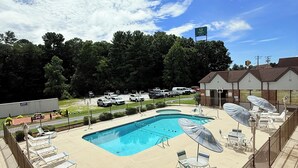 A pool area with lounge chairs and umbrellas, surrounded by a fence, with a building in the background.